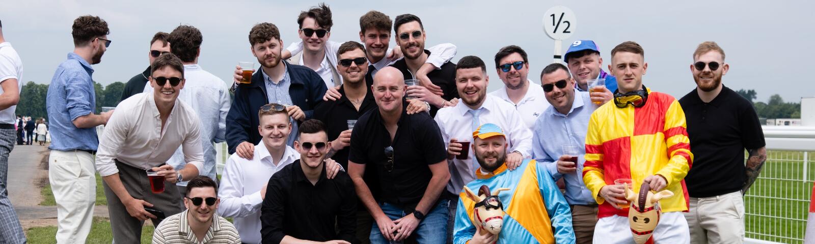A large stag party, with some dressed as jockeys posing for a picture at Worcester Racecourse